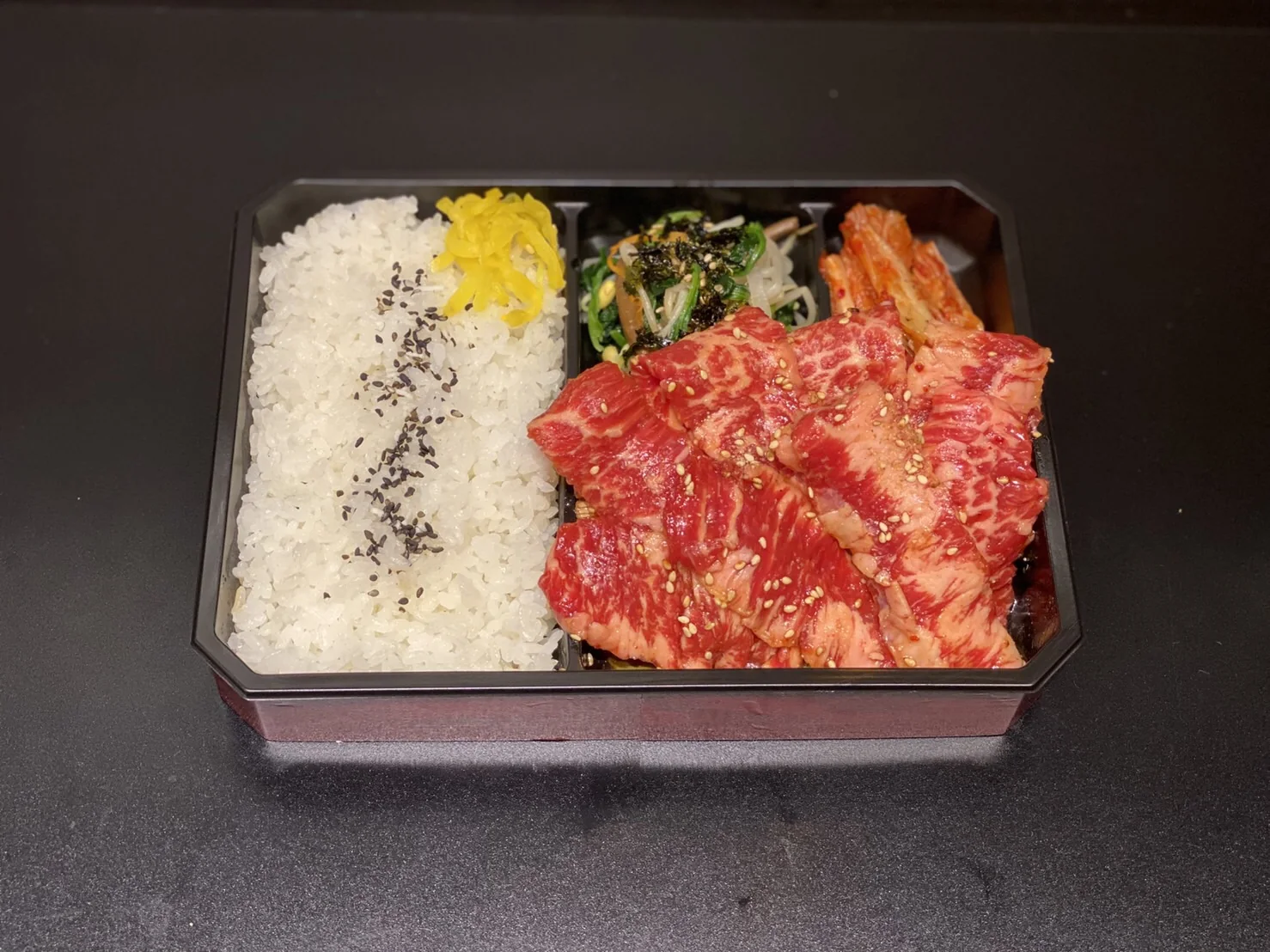 A takeout bento packed with rice, grilled meat, and kimchi